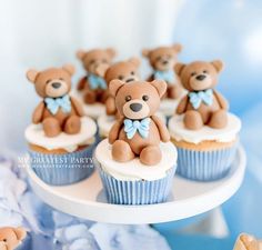 some cupcakes with teddy bears on them are sitting on a plate in front of blue and white decorations