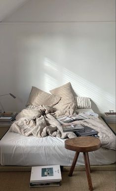 an unmade bed sitting in a bedroom next to a table with books on it