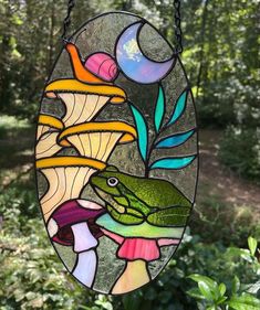 a stained glass window hanging from a chain in front of some plants and trees with the moon