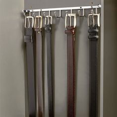 four belts are hanging on a wall with hooks