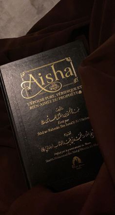 a black book with gold lettering sitting on top of a brown bed cover covered in blankets