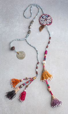 a necklace with beads and tassels on a white surface next to a coin