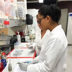 two women in white lab coats are working on some liquid and spoons at a laboratory counter