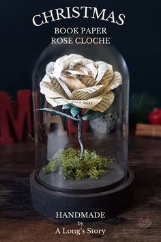 a fake rose under a glass dome on a wooden table with the title christmas book paper rose cloche