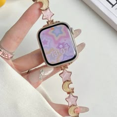 a woman's hand holding an apple watch with stars and moon charms