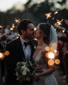 a bride and groom kissing with sparklers in the background