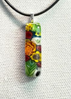 a glass pendant is hanging on a black cord necklace that has flowers and leaves painted on it