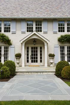 a large white house with blue shutters and potted plants on the front porch