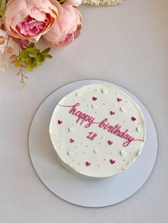 a birthday cake sitting on top of a white plate next to pink flowers and greenery