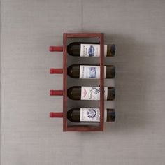 four bottles of wine are in a wooden holder on the wall next to a vase