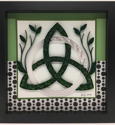 an intricate paper art piece with green and white designs on the front, in a black frame