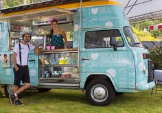 a man and woman standing in front of a blue food truck at an outdoor event