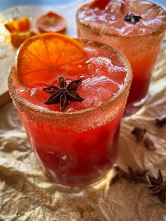 two cocktails with an orange slice and star anise sit on a tablecloth