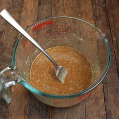 a glass bowl filled with brown liquid on top of a wooden table next to a measuring spoon