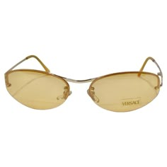 How stunning are these Versace dead stock sunglasses circa 1990s?! Perfect for anyone who loves an oval frame, the ones feature yellow lenses alongside light orange detailing with gold tone accents. These are the perfect every day sunglasses with an elevated touch of vintage! Match these to your favorite Chanel sun dress and pair with a Pucci handbag for a vibrant and retro-inspired look. Never been worn, new dead stock sunglasses in perfect condition, please see photos. Made in Italy. Luxury Gold Sunglasses, Yellow Lenses Sunglasses, Gold Sunglasses Aesthetic, 90s Style Sunglasses, Vintage Sunglasses Outfit, Bag Poster Design, Cool Clothing Brands, Tawny Autumn, Yellow Lens Sunglasses