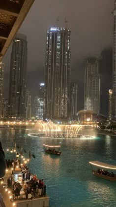 boats are in the water near some tall buildings at night with bright lights on them