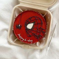 a spiderman birthday cake in a box on a white tablecloth with utensils