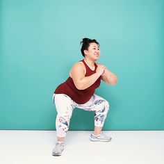 a woman is squatting in front of a blue wall with her hands behind her back