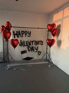 some red heart balloons are in front of a happy valentine's day sign on a wall