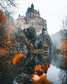 an old castle sits on top of a hill next to a body of water with trees in the foreground