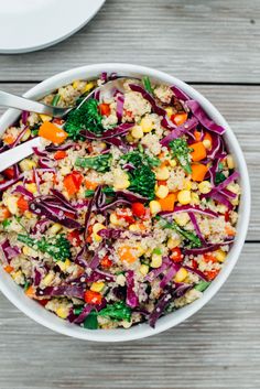 a white bowl filled with rice and vegetables on top of a wooden table next to a plate