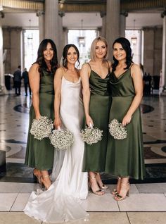 four bridesmaids in green dresses posing for a photo at the wedding reception with their bouquets