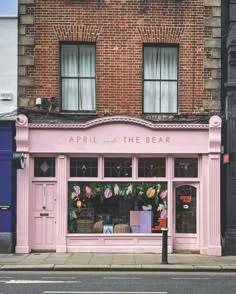 a pink store front on the side of a street with flowers hanging from it's windows