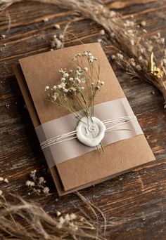 a small card with a button and flowers on it sitting on a table next to dried plants