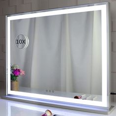 a white lighted vanity mirror sitting on top of a counter next to a vase with flowers