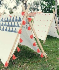 three teepees with red tassels are sitting in the grass