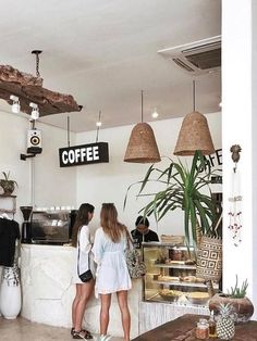 two women standing in front of a counter at a coffee shop with hanging lights above it