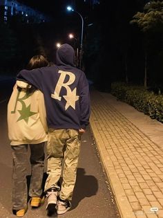 two people walking down the street at night with their arms around each other's back