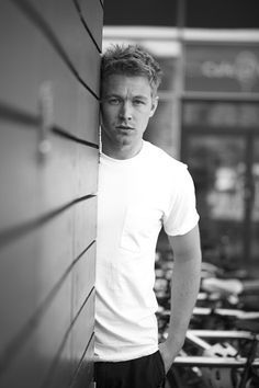 a black and white photo of a man leaning against a wall with his hands on his hips