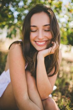 a beautiful young woman laying on the ground in front of trees smiling at the camera