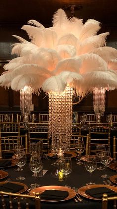 a tall centerpiece with white feathers on top of a black table cloth covered table