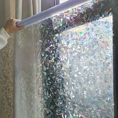 a person is holding up a curtain to look out the window with colorful glass shards on it