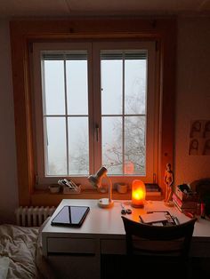 a desk with a laptop and a lamp on it in front of a large window