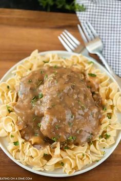 a white plate topped with pasta and meat covered in gravy on top of a wooden table