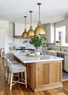 a kitchen with white counter tops and gold pendant lights over the island in front of it