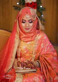 a woman in an orange and gold wedding outfit sitting on a couch with her hands together