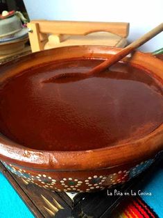 a wooden bowl filled with brown liquid on top of a blue table cloth next to a knife