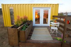 a yellow shipping container with plants and chairs on the deck next to an open door