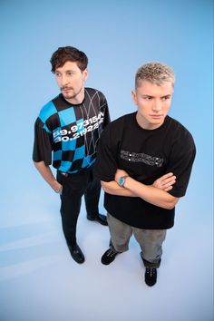 two men standing next to each other in front of a blue background with their arms crossed