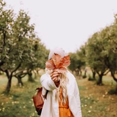 a woman holding an orange leaf in her hand while walking through an apple tree orchard