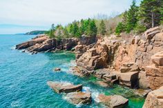 an aerial view of the ocean and rocky shoreline with trees on both sides, along with large rocks in the foreground