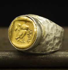 a gold coin ring sitting on top of a piece of silver and gold metal with the word aon engraved in it