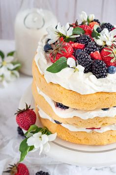 there is a cake with berries and cream on the top, next to a glass of milk