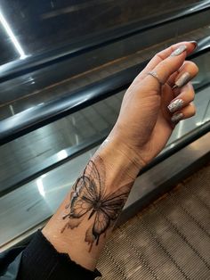 a woman's hand with a butterfly tattoo on her left wrist, and an escalator in the background