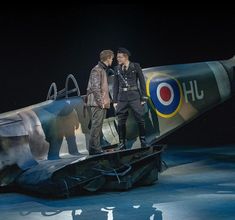 two men standing on top of an old plane in the dark with one man looking at another