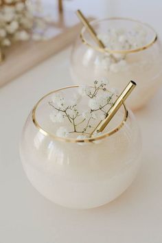 two white vases filled with flowers and gold straws on top of a table